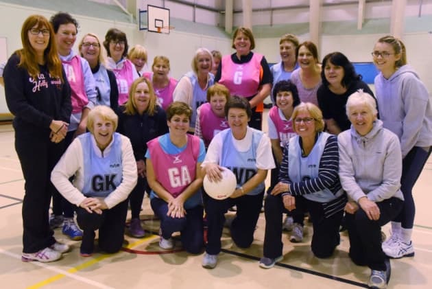 A walking netball group in bibs, kneeling and standing in a sports hall